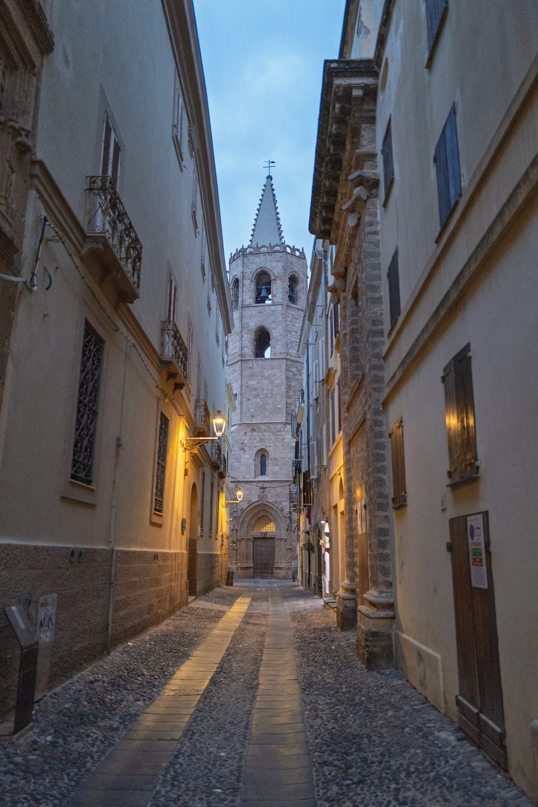 Vicolo lastricato del centro storico di Alghero con il campanile ottagonale della cattedrale di Santa Maria al tramonto