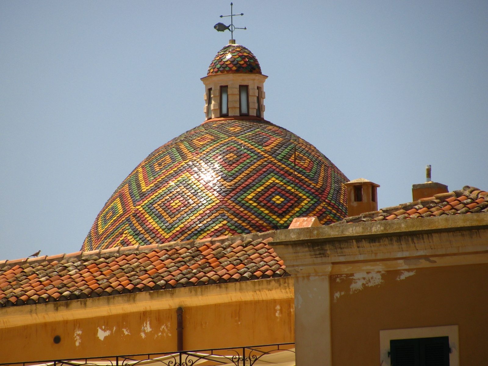 La cupola rivestita di maioliche policrome della chiesa di San Michele che spunta sopra i tetti del centro storico di Alghero