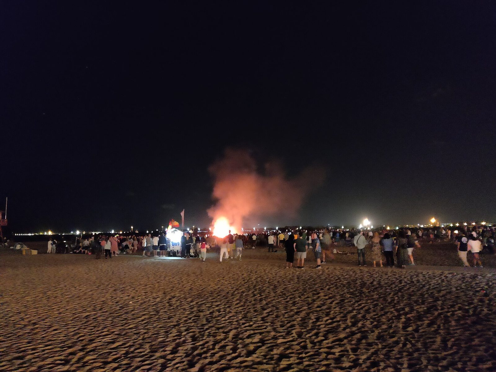 Un grande falò acceso su una spiaggia nella notte di San Giovanni, con le persone raccolte intorno al fuoco