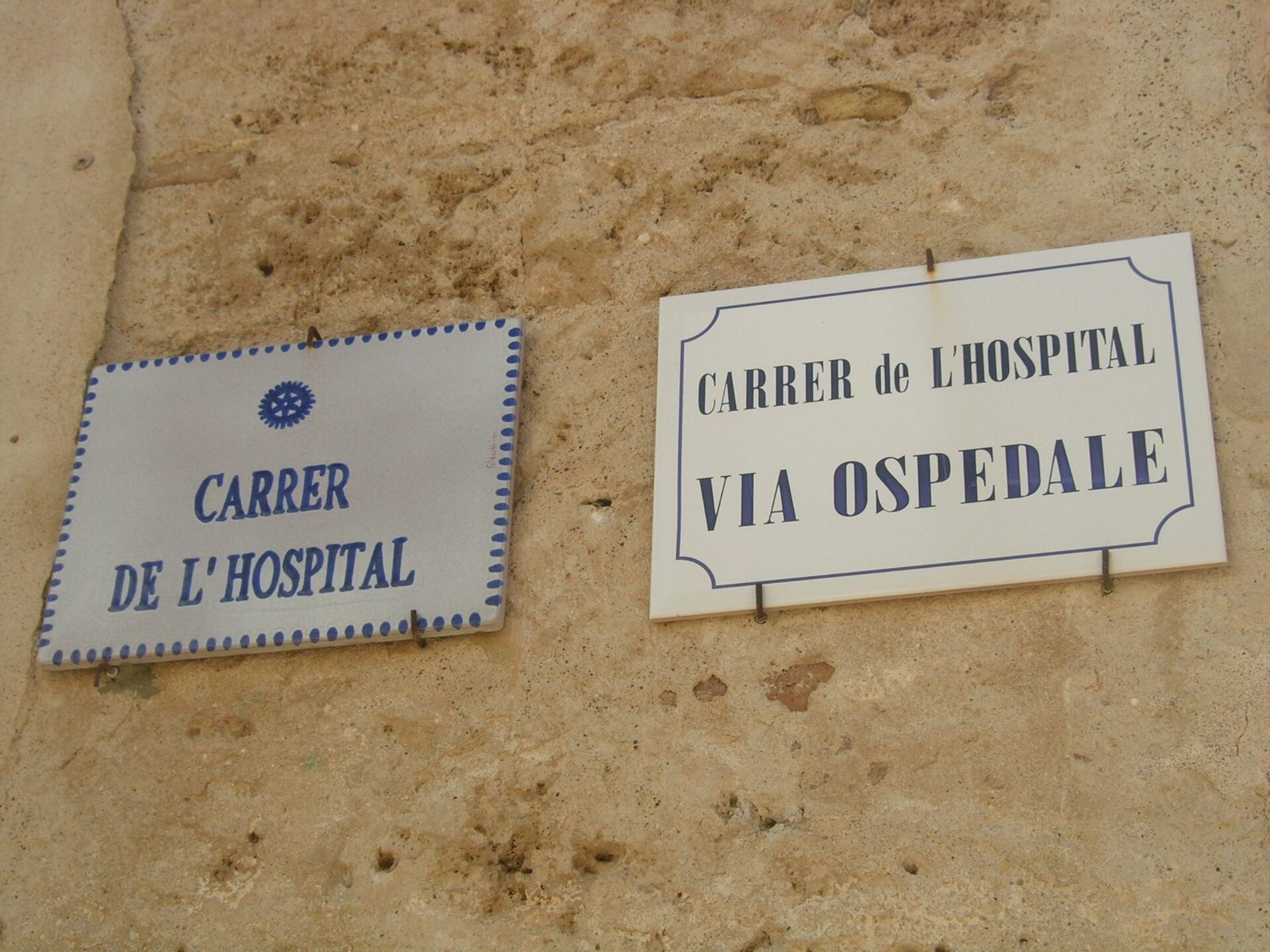 Targhe stradali bilingui ad Alghero: Carrer de l'Hospital e Via Ospedale su un muro in pietra