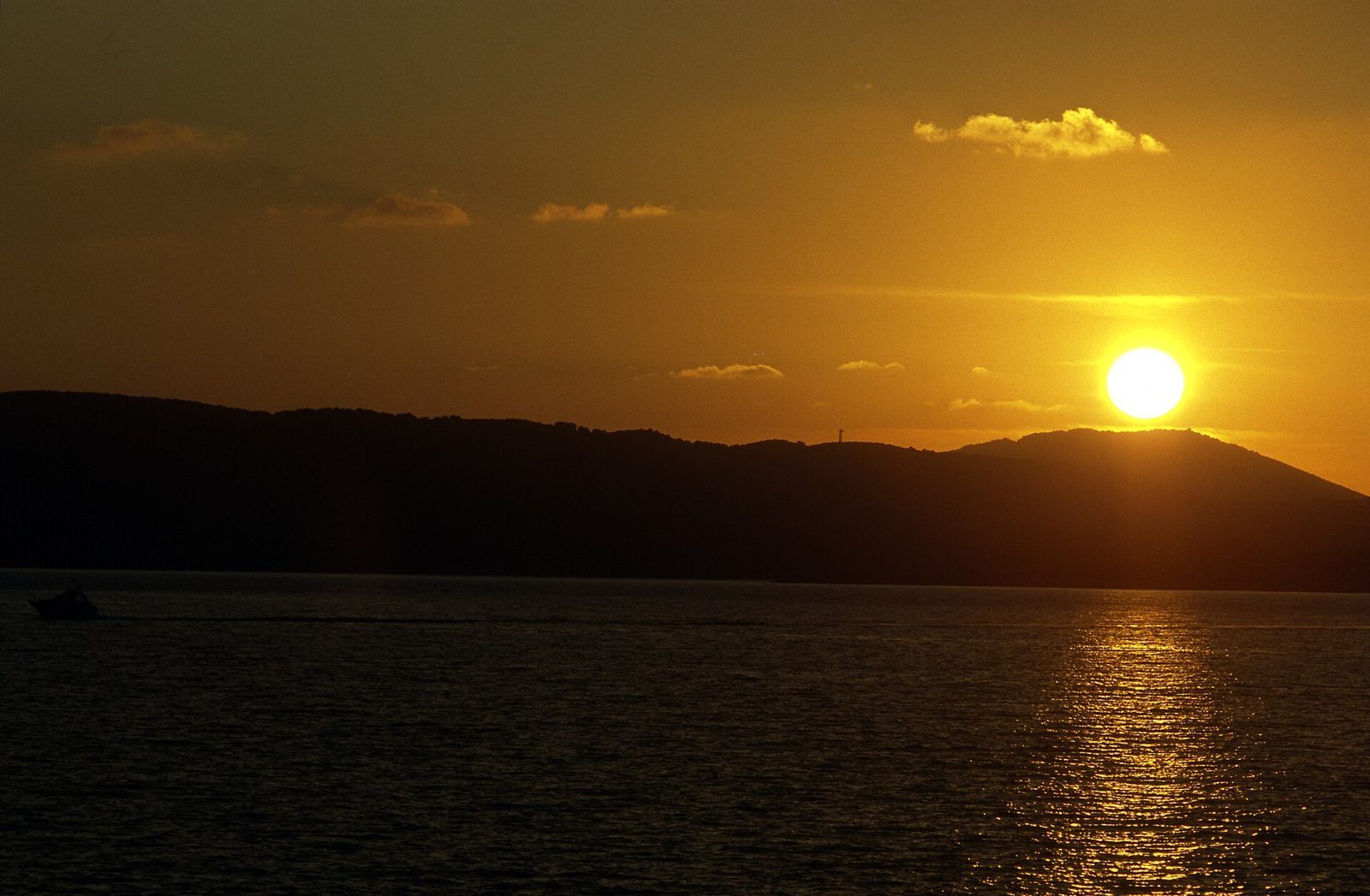 Tramonto dorato sul golfo di Alghero con il profilo scuro delle colline sul mare